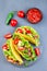 Taco shells on stone plate, with lettuce, ground beef meat,  mashed avocado, tomato, red onion and jalapeno pepper, vertical, top