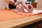 Tailor at work. Close-up of a dressmaker`s hands transferring sewing patterns for clothes on orange colored satin fabric in