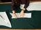 Tailor worktable in studio. Female hands making chalk markings of paper patterns on green fabric.