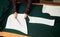 Tailor worktable in studio. Female hands making chalk markings of paper patterns on green fabric.