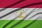Tajikistan flag is depicted on a sports cloth fabric with many folds. Sport team banner