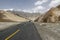 Take a low-angle photograph of a newly built straight asphalt road leading to the foot of a distant mountain