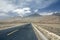 Take a low-angle photograph of a newly built straight asphalt road leading to the foot of a distant mountain