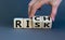 Take a risk and getting rich concept. Hand flips a cube and changes the word `risk` to `rich` or vice versa. Beautiful grey