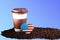 Takeaway ceramic cup and coffee beans on blue background