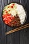 Takoraisu dish consists of ground beef, cheese, lettuce, and tomatoes served on a bed of short grain rice close-up in a bowl.