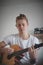 Talented boy playing a wooden acoustic guitar in a lighted room. Blonde Man aged 20-29 strums guitar and sings from hymn book on