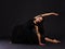A talented girl gymnast, in a black dress, sits in a half-string and bends back. Black background.