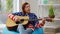 Talented mature woman singing playing guitar sitting on bag chair indoors at home. Portrait of skilled confident