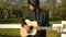 Talented Middle Eastern male musician playing guitar singing leaning on wooden fence in summer park. Portrait of skilled