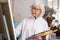 Talented retired woman painting standing near canvas