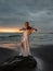 Talented woman with violin on the beach. Music and art concept. Slim girl wearing long white dress and playing violin in nature.