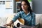 Talented young woman holding guitar in hands at home