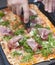 Talian pizza with arugula and ham. Delicious traditional food for lunch. The hand cuts the pizza into portions. Homemade baking.