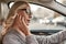 Talking with client. Portrait of attractive woman in eyeglasses adjusting headphones while driving a car