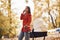 Talking by the phone. Mother in red coat have a walk with her kid in the pram in the park at autumn time