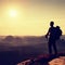 Tall backpacker with poles in hand. Sunny daybreak in mountains. Hiker with big backpack on rocky view point above misty valley.