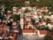 Tall bell tower of the Church of St. Nicholas with a clock among the red roofs of old houses. Perast, Montenegro. Drone