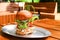Tall big tasty beef burger or hamburger on metal plate on wooden table in outdoor street cafe. Having brunch on sunny day,