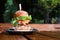 Tall big tasty hamburger or beef burger on black plate on wooden table in street cafe. Having brunch on sunny day, fastfood. Copy
