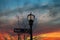 A tall black metal lamp post with street signs surrounded by bare winter trees with blue sky and powerful red clouds