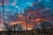 Tall black town cranes at a construction site surrounded by lush green and bare winter trees with powerful red clouds in the sky