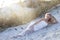 A tall blond woman laying in the sand with floral wreath on her head.