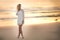 A tall blond woman walking on the beach at sunrise.