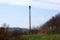 Tall cell phone metal antenna tower next to railroad with multiple electrical poles surrounded with uncut green grass and dense