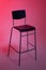 A tall chair stands in a photo studio on a white paper background lit in pink tones