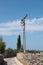 Tall concrete pole with electric wire in countryside. Narrow road with stone wall. Blue sky with white clouds.