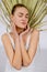 Tall European young woman with blonde hair in bun in white singlet, against background of palm leaf on white background