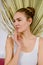 Tall European young woman with blonde hair in bun in white singlet, against background of palm leaf on white background