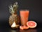 A tall faceted glass of a mixture of fruit juices on a black background, next to pieces of ripe pineapple and grapefruit