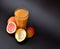 A tall faceted glass of a mixture of fruit juices on a black background, next to a ripe mango and half a grapefruit