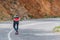 Tall fit male longboarder riding his longboard downhill on a sunny day high in nature while wearing a red shirt, green hat, and