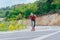 Tall fit male longboarder riding his longboard downhill on a sunny day high in nature while wearing a red shirt, green hat, and