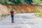 Tall fit male longboarder riding his longboard downhill on a sunny day high in nature while wearing a red shirt, green hat, and