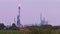 Tall gas flare of refinery plant near green field