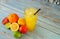 A tall glass cup of citrus juice with ice and a straw, stands on a table in a pile of whole and chopped oranges, lemons, lime and