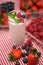 Tall glass with fresh yoghurt, mint and berries. With arranged berries in the background. On red and white checkered tablecloth