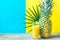 Tall Glass with Freshly Pressed Pineapple Orange Coconut Juice Straw Flower. Round Palm Leaf on Duotone Blue Yellow Background