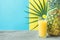 Tall Glass with Freshly Pressed Pineapple Orange Coconut Juice Straw and Small Flower. Round Palm Leaf on Blue Yellow Background