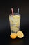 A tall glass of refreshing lemonade with ice and citrus pieces on a black background
