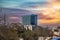 A tall glass skyscraper in the cityscape surrounded by other buildings, lush green trees and bare winter trees