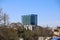 A tall glass skyscraper in the cityscape surrounded by other buildings, lush green trees and bare winter trees with clear blue sky