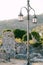 A tall gray street lamp among ancient stone ruins, hills and green vegetation.