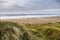 Tall green grass on a dune. Fanore beach in the background. County Clare, Ireland. Cloudy sky over the ocean. Travel and landmark