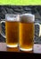 Tall half-liter glasses of light chilled beer with cool foam on a wooden desk at outdoor pub