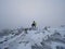 Tall hiker in black on peak of the world . Heavy orange mist bellow in valley.